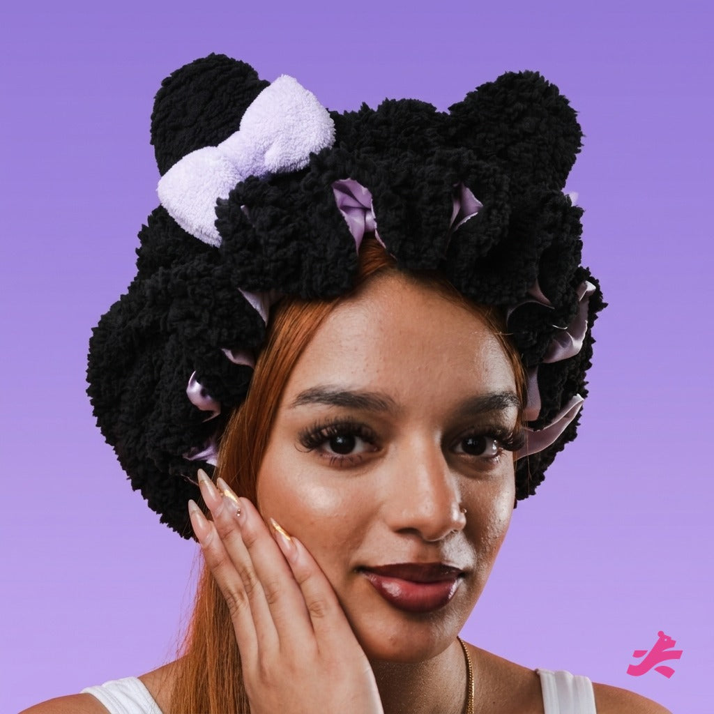 Black plush teddy bonnet with lilac bow, hand on cheek, on lilac